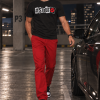 Man draagt het zwarte #STOUT Cutout Kiss T-Shirt met volledige wit-rode print in een parkeergarage